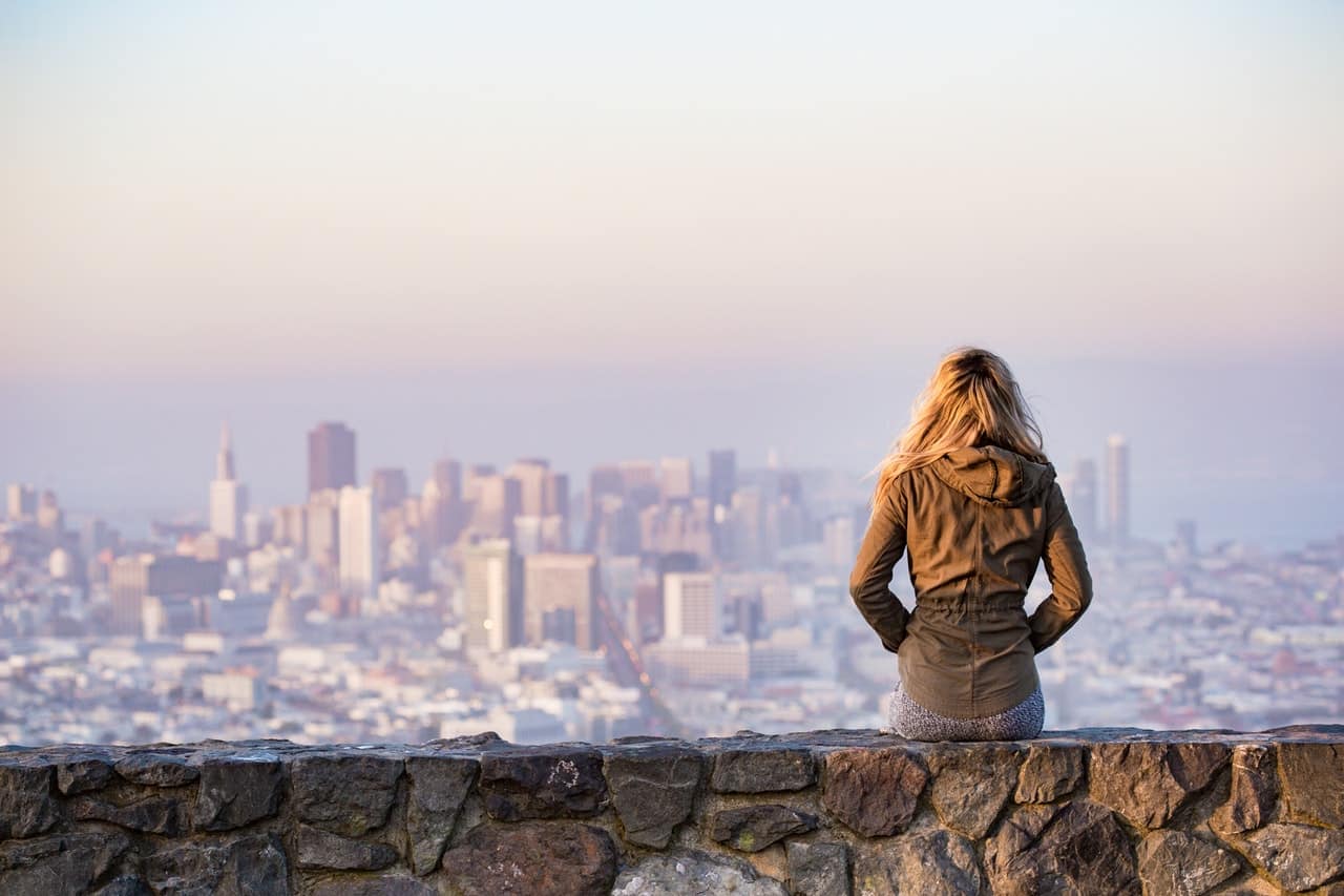 A woman sitting on top a stone wall and looking over the city