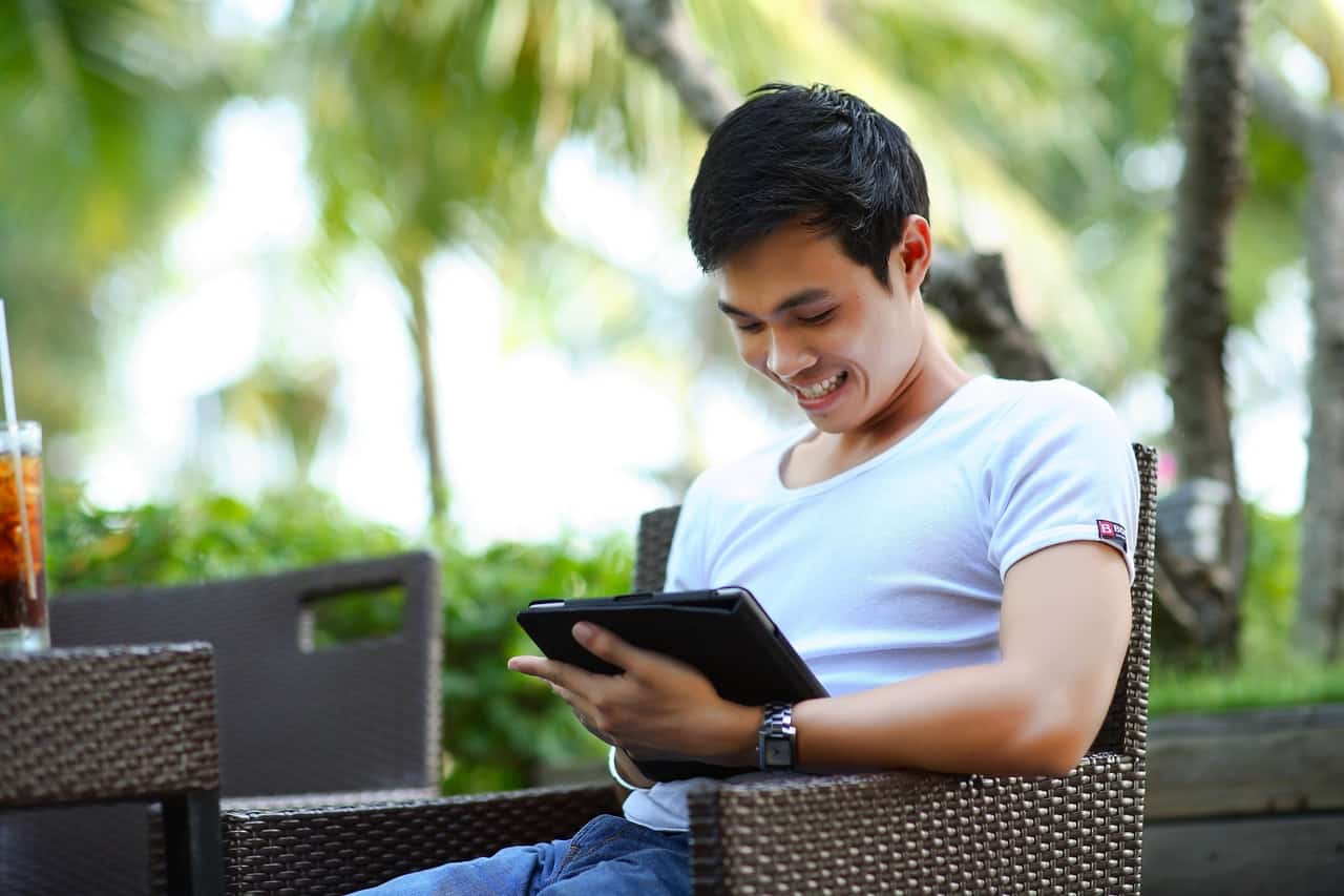 An asian man looking at his tablet and smiling