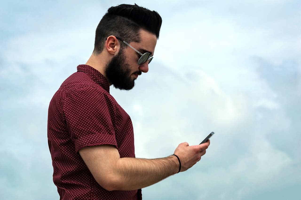 A man with sun glasses looking down at his phone